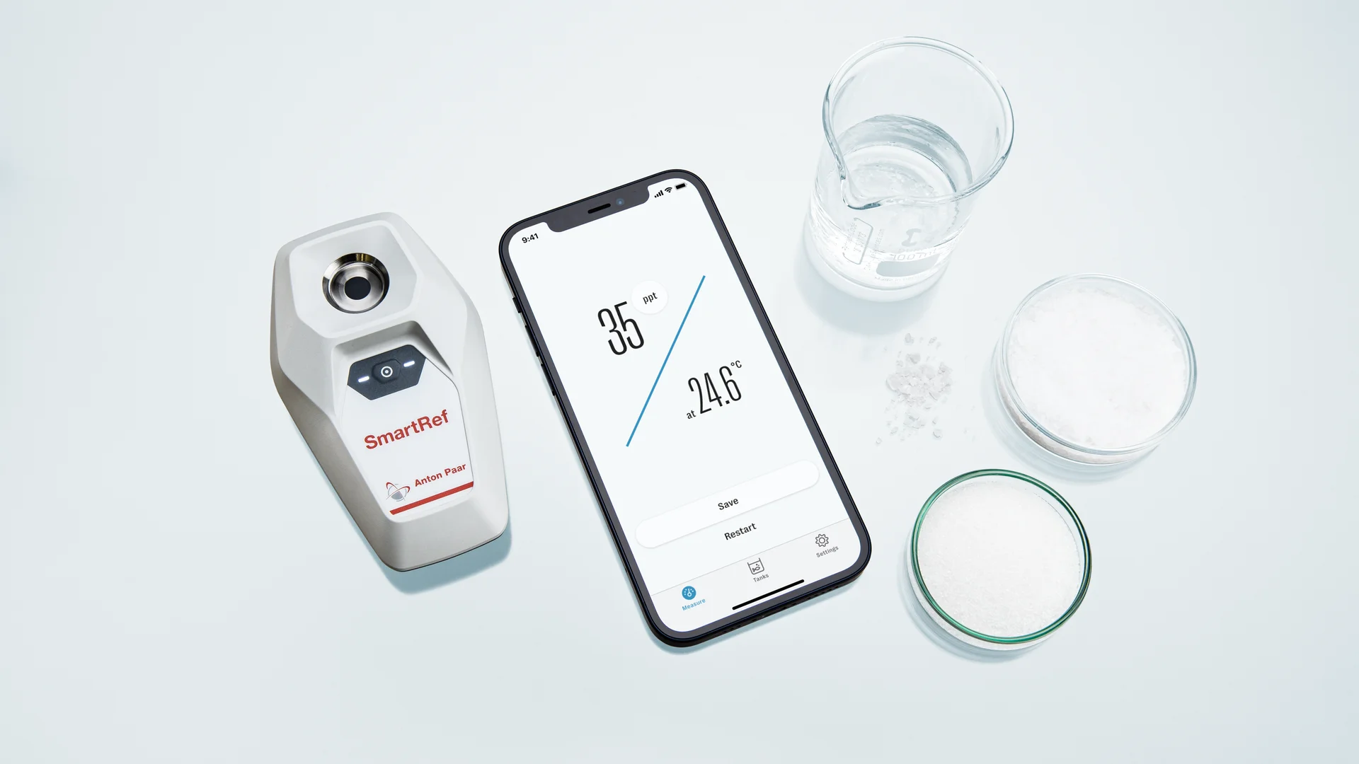 Handheld digital refractometer beside a phone showing a salinity reading of 35 ppt at 24.6 degrees C